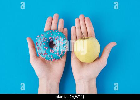 Frau zwischen Apple und Krapfen, die beschließen, in ihre Hände. Gesunde Ernährung Konzept Stockfoto