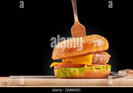 Handwerk Burger mit Gabel auf schwarzem Hintergrund. Auf Platte Cheeseburger. Stockfoto