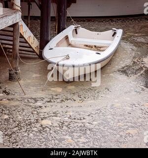 Eine kleine weiße Zeile boot gebunden bis zu einem Post in wirbelnden schaumig schmutziges Wasser in einem alten Fachwerkhaus Bootsanleger mit Müll beladen Stockfoto