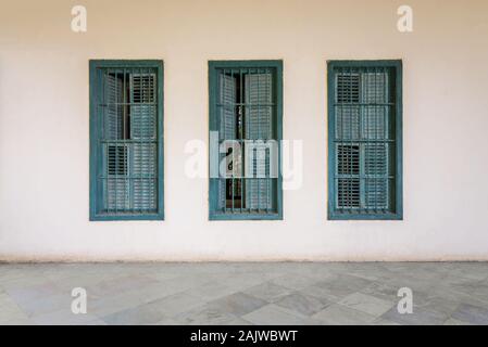 Weiße Wand mit drei grunge Windows mit grünen Fensterläden und schmiedeeisernen Bars und weißem Marmorboden Stockfoto