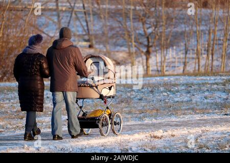 Paar mit einem Baby Stroller Walking im Winter Park während der. Schneewetter, Konzept der Mutterschaft, Eltern mit Kinderwagen Stockfoto