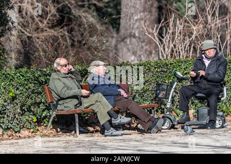 Drei sitzen alte Männer Chat auf eine Bank und eine Invalidität scooter im El Retiro Park, Madrid, Spanien Stockfoto