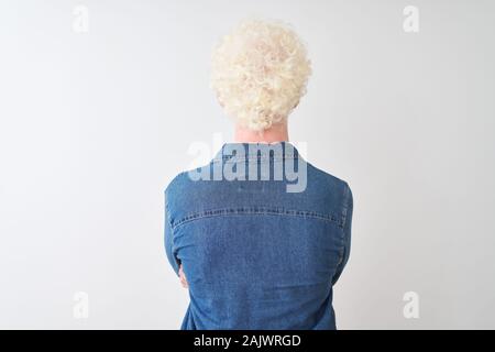 Junge albino blonder Mann tragen Jeanshemd und Gläser über isoliert weißer Hintergrund stehen nach hinten weg schauen mit verschränkten Armen Stockfoto
