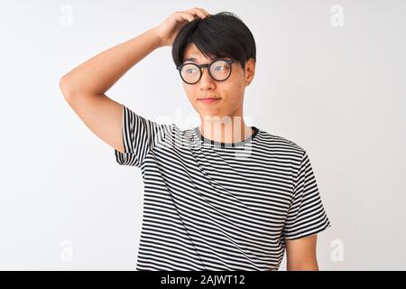 Chinesischer Mann mit Brille und Marine gestreiftes T-Shirt stehend über isoliert weißer Hintergrund verwechseln und frage mich. Unsicher mit Zweifel, Stockfoto