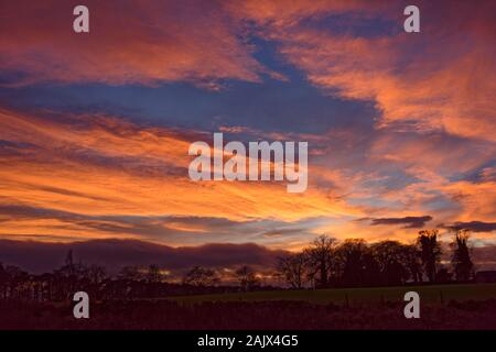 Dramatische Orange und rote Wolken beleuchtet durch die Einstellung im Winter Sonnenuntergang über die Felder und die ländliche Lage der Colliston Dorf in Angus. Stockfoto