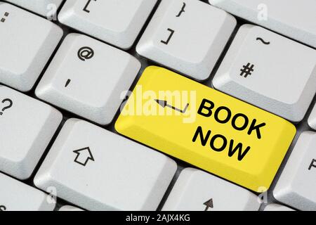 Eine Tastatur mit Buch, die jetzt in schwarzer Schrift auf einer gelben ENTER-Taste geschrieben ist. Online Urlaub buchen. England, Großbritannien, Großbritannien Stockfoto