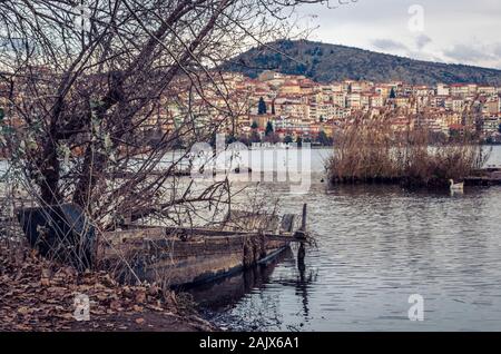 Blick auf die Stadt Kastoria und den See Orestiada bei Sonnenuntergang. Verlassenes Holzboot im Vordergrund. Stockfoto