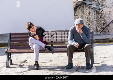 Capileira, La Alpujarra, Alpujarras, Granada, Andalusien, Spanien. Eine Jugend spielt auf seinem Handy Neben ein älterer Mann im Dorf Sitzung Stockfoto