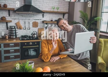 Jungen gutaussehenden Mann im grauen Hemd und seine Mama in Videoanrufe mit Freunden Stockfoto