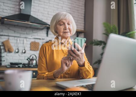 Gut aussehende ältere Dame in Gelb auf der Suche beteiligt Stockfoto