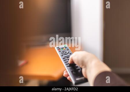 Hand zeigen einer TV-Fernbedienung auf den Fernseher. Zeit, um fernzusehen. Die Fernbedienung in der Hand. Für text Stockfoto