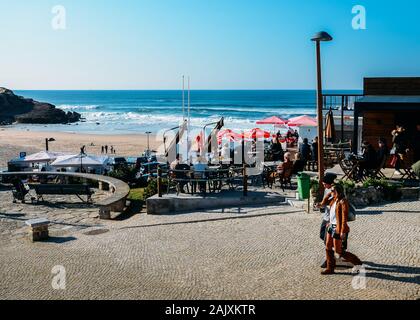 Sintra, Portugal - Jan 5, 2020: die Menschen in einem Café mit Blick auf den goldenen Praia das Macas in Portugal an einem sonnigen Wintertag entspannen Stockfoto