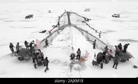 Chinesische Arbeiter ziehen einen riesigen fischernetz Eine gute Ernte auf dem zugefrorenen See in Wolong Kangping County, Shenyang City zu erwarten, im Nordosten Chinas Liaon Stockfoto