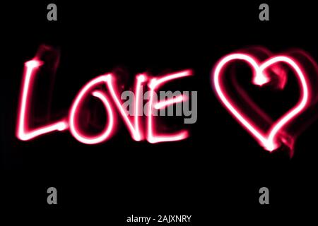 Wort Liebe weiß ein Herz in Pink auf schwarzen Hintergrund. Licht Malerei. Stockfoto