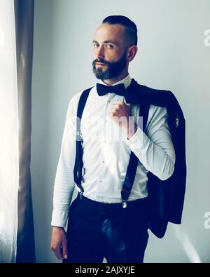 Eleganten Mann mit einer Jacke über die Schulter schauen aus dem Fenster Stockfoto