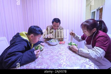 (200106) - chongqing, Januar 6, 2020 (Xinhua) - Lief Guanghui (C) Abendessen mit seiner Frau Qu Guangfang und ihr Sohn lief Junchao zu Hause im Südwesten Chinas Chongqing Gemeinde, Jan. 5, 2020. Lief Guanghui, 50, hat sein Leben als 'Bang Bang', buchstäblich 'Tick', in Chongqing seit zehn Jahren erwarb. In einer bergigen Stadt Chongqing mit einer Fülle von hügeligen Straßen und Wege, stick Männer haben unterstützt Menschen, die von Gepäck und schwere Sachen. Schleppen waren auf Bambusstangen auf ihren Schultern ausgeglichen, der Stick Männer verdienten Brot im Schweiße Ihrer Augenbrauen. Einer von ihnen wurde Lief Stockfoto