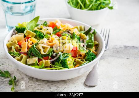 Valentinstag essen Konzept. Salat mit Pasta Herz, Oliven, Tomaten, Spinat und Brokkoli in einer weißen Schüssel. Stockfoto