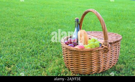 Outdoor Picknick am sonnigen Tag Picknickkorb mit einer Flasche Rotwein, Baguette, weißen und schwarzen Weintrauben und Äpfel Rattan Picknickkorb mit weißen und bla Stockfoto