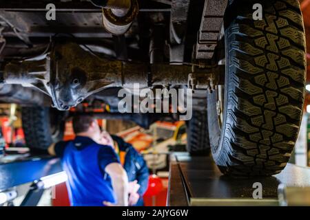 Riga, Lettland - 12 April 2019: ein Mechaniker prüft die technischen Stand unter einem angehobenen Auto auf einer Brücke in einer Garage - Bild Stockfoto