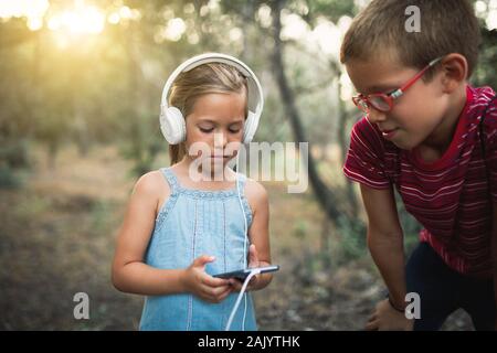 Zwei Kinder hören von Musik im Wald mit Kopfhörern Stockfoto