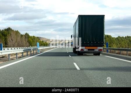 Lkw auf der Autobahn zwischen Bäumen mit dem dunklen Grün Canvas Stockfoto