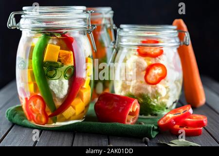 Drei Gläser von fermentierten Blumenkohl, Gurken, Möhren, Chili, Gewürze, Salz. Gemüse auf einem dunklen Hintergrund. Über textile Grün. Ferme Stockfoto