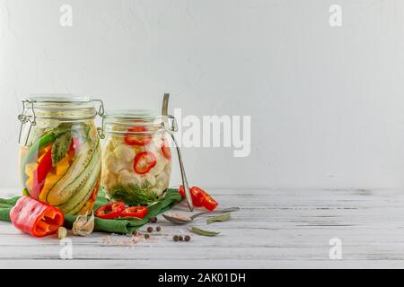 Zwei Gläser von fermentierten Blumenkohl, Gurken, Zwiebeln, Gemüse auf einem hellen Hintergrund. Über textile Grün. Gärung ist eine Quelle von probiot Stockfoto