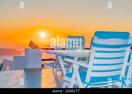 Santorini sunset von im Außenbereich Terrasse mit Gartenmöbeln in Weiß und Blau unter Golden Sky die Sonne untergeht. Stockfoto