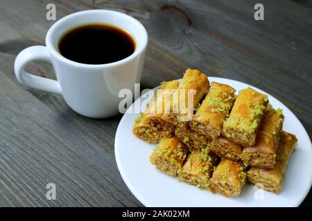 Platte von Pistazien Baklawa Gebäck mit einer Tasse türkischen Kaffee serviert auf hölzernen Tisch Stockfoto