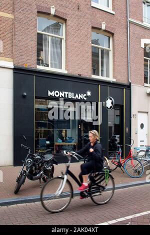Blick auf Frau Reiten Fahrrad in verschwommene Bewegung in Store Front Deutscher Schreibgeräte Hersteller auf Luxus Shopping Straße namens 'Pieter Corne Stockfoto