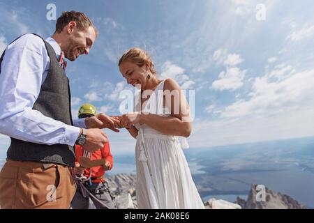 Braut setzt Ring auf dem Finger des Bräutigams während der Berggipfel Hochzeit, Wyoming Stockfoto