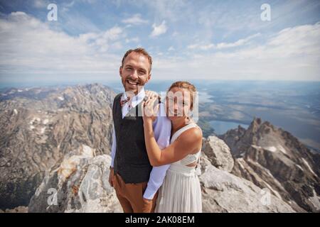 Glückliche Braut und Bräutigam lächeln auf Berggipfel nach der Hochzeit Stockfoto