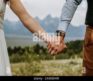 Braut und Bräutigam halten die Hände vor Grand Teton, Wyoming Stockfoto