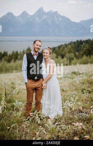 Brautpaar und Brautpaar halten sich im Blumenfeld Stockfoto