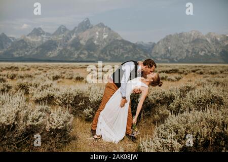 Bräutigam taucht Braut für Kuss im Feld vor Grand Teton, Wyoming Stockfoto