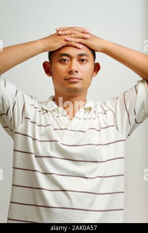 Portrait von asiatischen ethnischen jungen männlichen Erwachsenen gelegt, die Hand an den Kopf, entspannend Stockfoto
