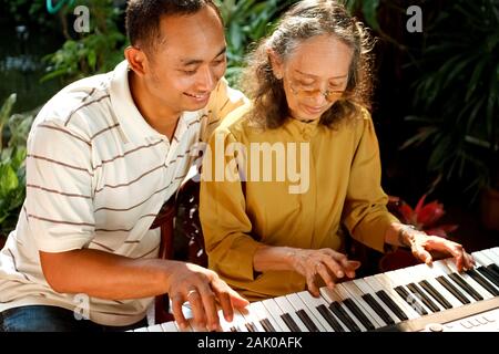 Asiatische ethnischen Familie Portrait von älteren Mutter Klavier spielen, von ihrem Sohn begleitet Stockfoto