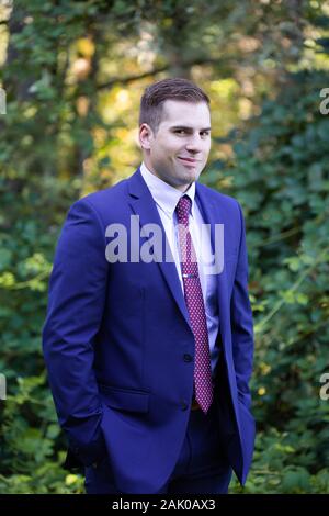Junger Mann im Business-Anzug schmunkelt vor der Kamera im Freien. Stockfoto