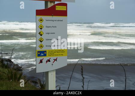 Ein Schild warnt Schwimmer und Strandgänger vor gefährlichen Gefahren am Muriwai Strand, Neuseeland, einem der gefährlichsten Strände Neuseelands. Stockfoto