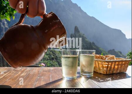 Man gießt Weißwein aus Ton Kanne in Glas auf der Terrasse mit Blick auf die grüne Landschaft der kleinen Bergdorf Masca auf Teneriffa, Spanien im sonnigen d Stockfoto