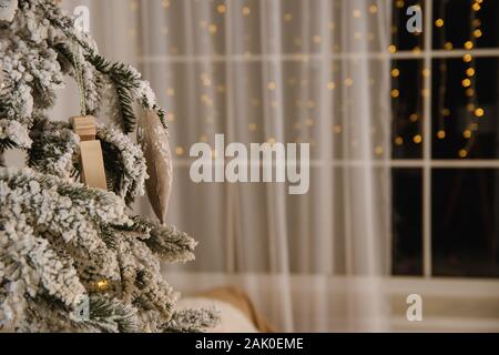 Weihnachtsbaum mit Spielsachen eingerichtet und steht in der Nähe der Fenster am Abend, wo eine Girlande mit Bokeh leuchtet. Stockfoto