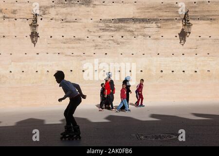 Tradition und Moderne - Junge auf Inline-skates und Fußgänger (Frauen und Kinder) am Nachmittag Landschaft der Stadtmauer in Fes (fès), Marokko Stockfoto