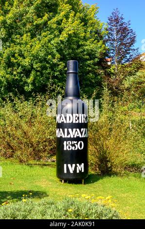 Santana, Madeira, Portugal - Sep 24, 2019: Riesige Flasche Wein Madeira Wein als Exponat auf Madeira Themenpark. Große schwarze Flasche Wein im Freien umgeben von grünen Bäumen. Vertikale Foto. Stockfoto