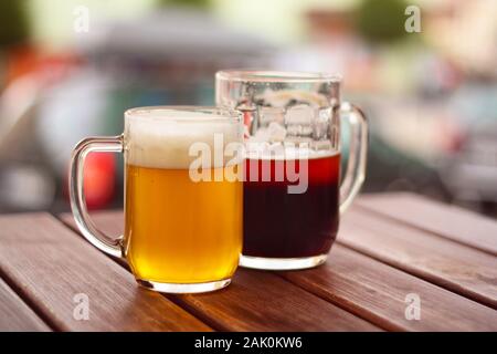 Bier auf dem Tisch: Zwei Gläser Bier auf einem Holztisch auf der Terrasse des Restaurants, kleines helles Bier und dunkles Bier in Pint, unscharfer Hintergrund Stockfoto