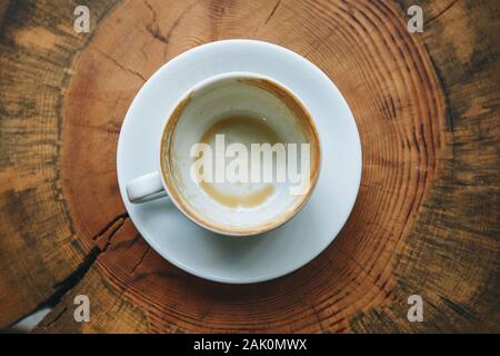 Blick von oben auf eine leere weiße Tasse nach dem Trinken von Kaffee auf einem Holztisch. Konzept für die Beendigung einer Sitzung oder etwas anderes. Stockfoto