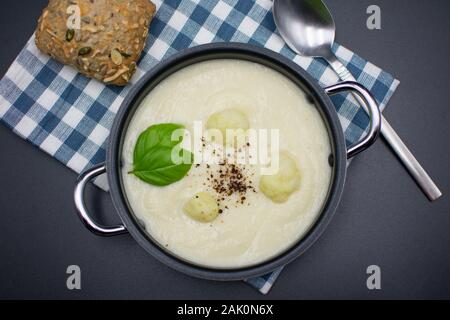 Blumenkohl Suppe im Topf mit karierten Serviette und bun auf schwarzem Hintergrund. Ansicht von oben Stockfoto