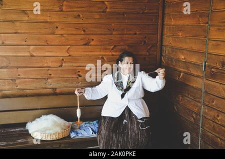 Santana, Madeira, Portugal - Sep 24, 2019: Frau in traditioneller Tracht sitzt auf einer Holzbank und hand Spinnen von Wolle. Altes Handwerk, Handwerk. In Madeira Themenpark. Stockfoto