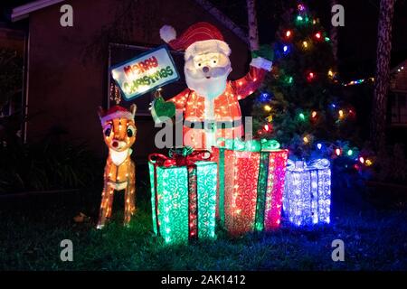 Beleuchtete Weihnachtsdekorationen, Weihnachtsmann, Rentier, Geschenke, vor einem Haus angezeigt; Nachtansicht Stockfoto