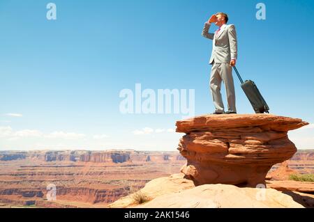 Geschäftsmann, der mit einem Rollie-Handtasche steht und auf die massive Landschaft des roten Felsens blickt Stockfoto