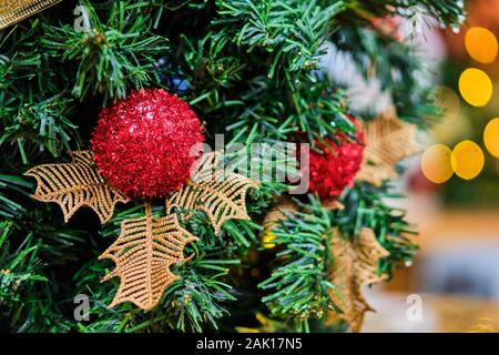 Christbaumschmuck in Form einer roten Kugel auf einem Zweig eines Baumes. Unscharfer Hintergrund mit Beleuchtung. Close Up. Stockfoto